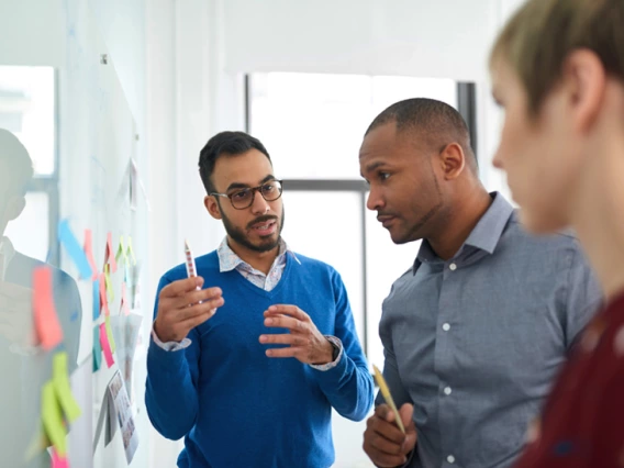 3 people talking near a whiteboard